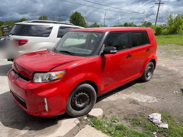 Red Scion xB with front-end collision damage parked at the shop